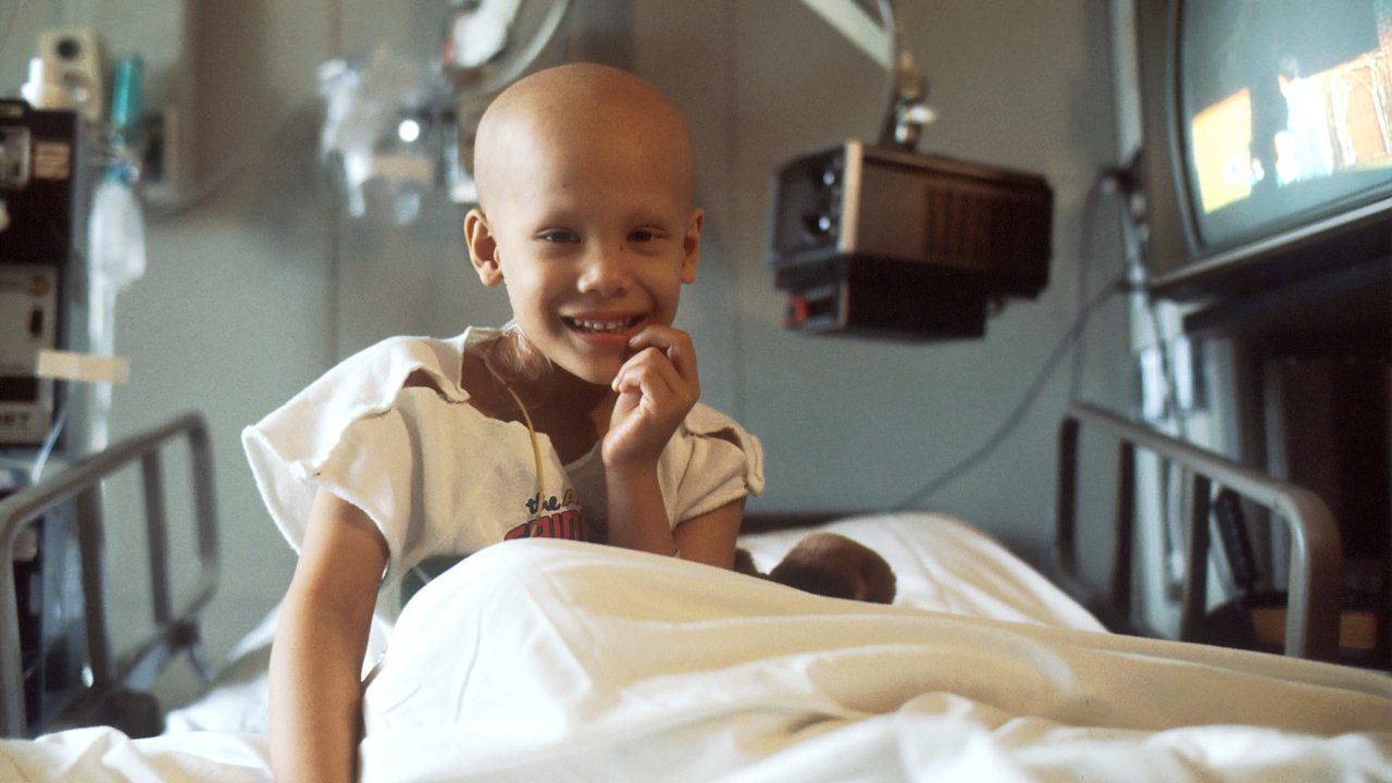 Foto de criança careca em cama, com câncer infantil