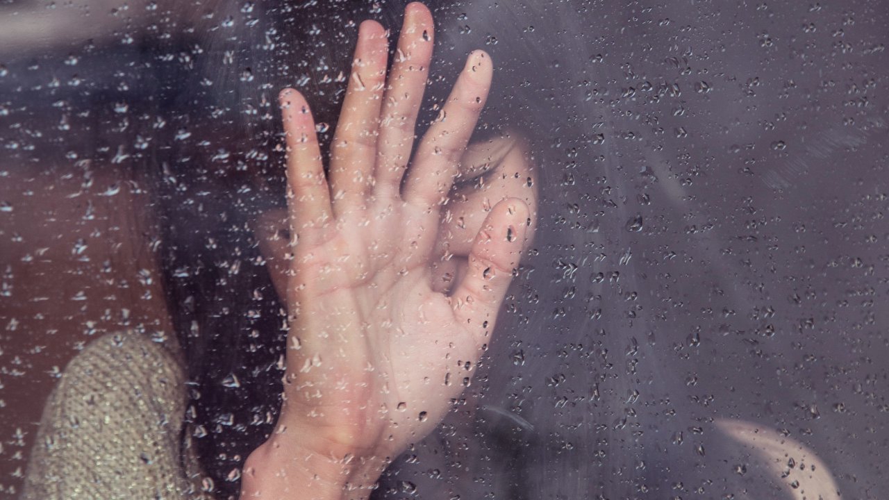 Mulher triste colocando a mão em uma janela molhada