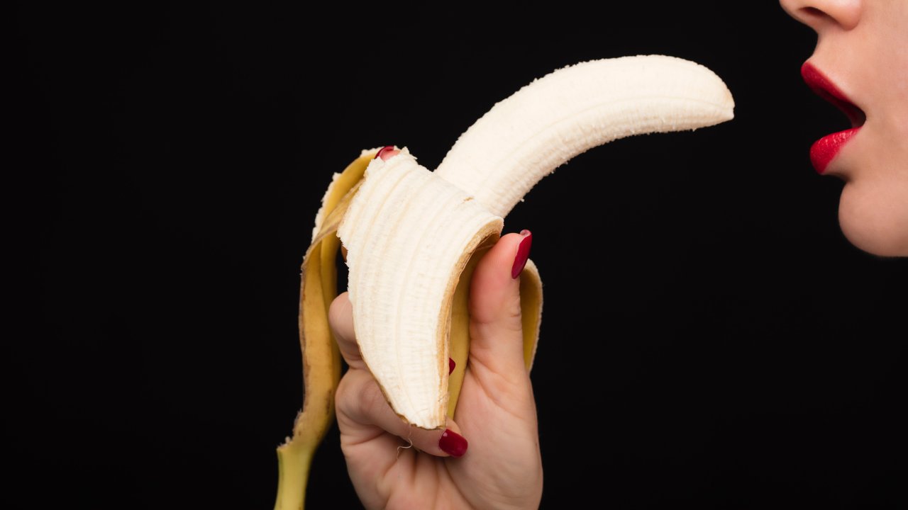 Foto de mulher segurando uma banana na frente da boca, em alusão ao sexo oral.