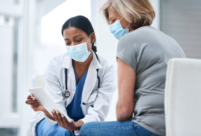 Médica e paciente lado a lado, ambas de máscara