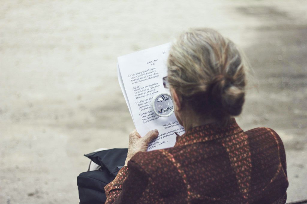 Mulher idosa lendo com lente de aumento