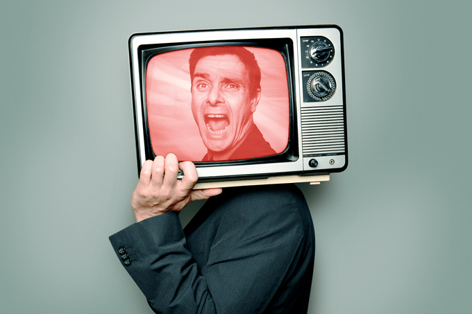 Foto de homem segurando uma televisão na altura do rosto.