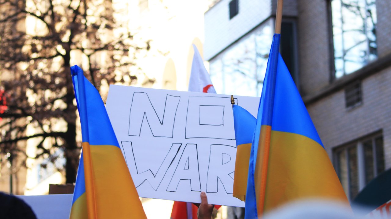 Foto de manifestação em que há um cartaz com os dizeres "No War" e bandeiras da Ucrânia