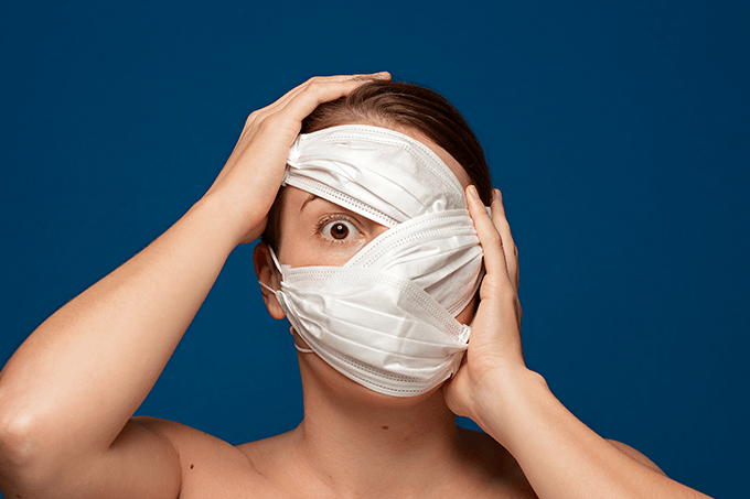 Foto de mulher com máscaras cobrindo o rosto e expressão de assustada, simbolizando que Covid causa depressão e ansiedade