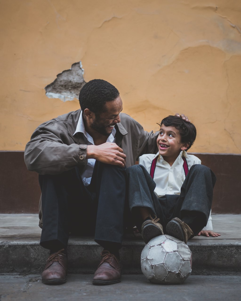 Foto de homem ao lado de criança que está com bola de futebol no pé, simbolizando dia dos pais.