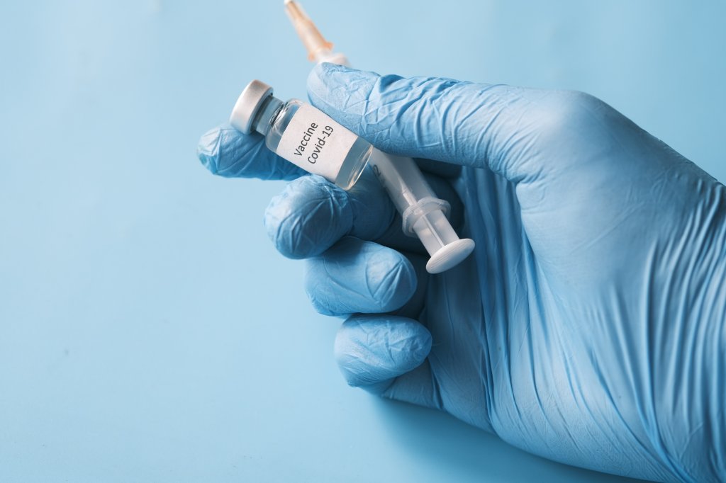 Mão segurando ampola e injeção com vacina da covid