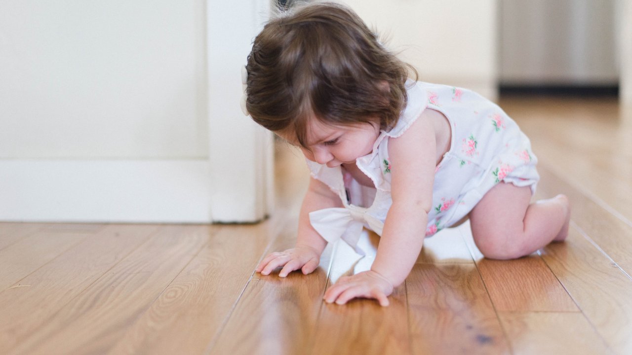 Criança engatinhando em chão de madeira