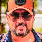 Homem de boné, óculos escuros, barba e bigode