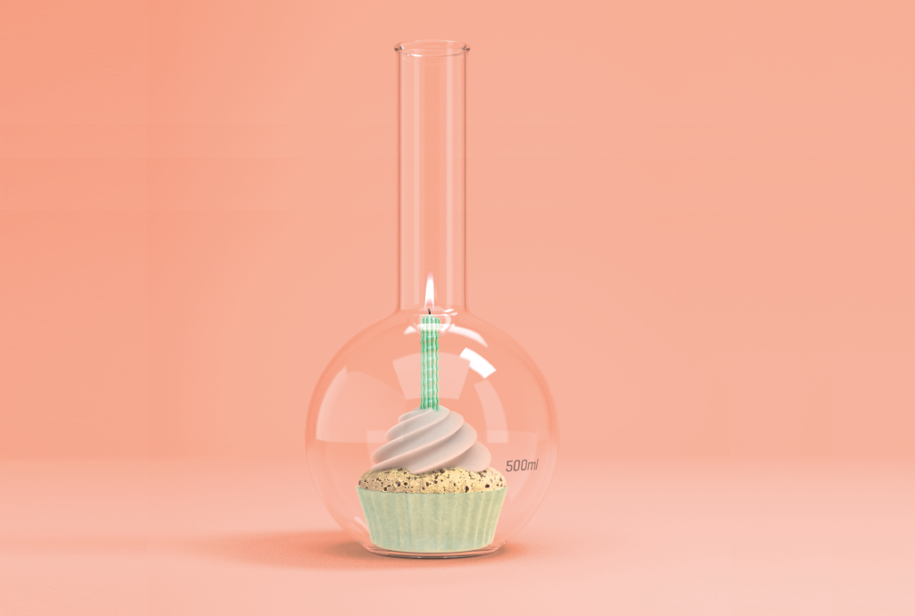 Um cupcake com cobertura rosa e forminha verde-clara, com uma vela verde acesa, dentro de um balão de fundo redondo de vidro, sobre um fundo rosa-pêssego. O balão tem uma marcação de 500ml no lado direito
