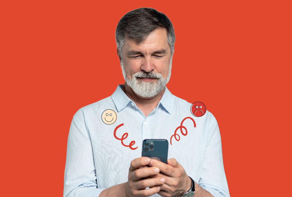 Homem de barba grisalha e camisa azul clara, olhos fechados, segurando um smartphone. Ícones de rosto feliz e triste com linhas vermelhas em espiral indicam emoções conflitantes ao usar o aparelho