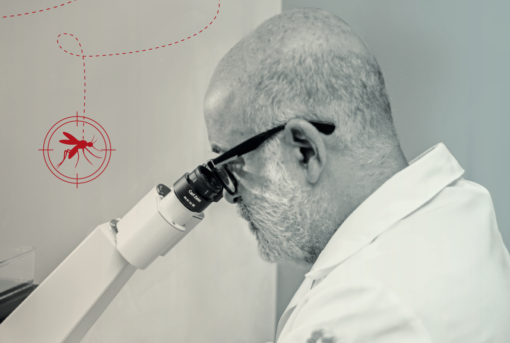 Cientista careca e barbudo, de óculos e jaleco branco, observa através de um microscópio. No canto superior esquerdo, um mosquito vermelho dentro de uma mira, conectado por uma linha pontilhada